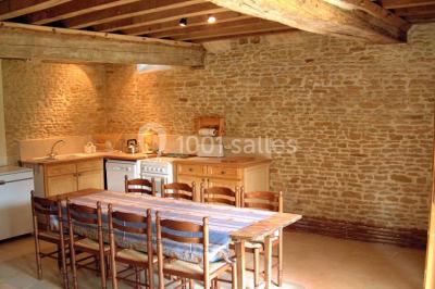 Salle à manger rustique avec murs en pierre, table en bois, chaises assorties et porte-fenêtre donnant sur l'extérieur.