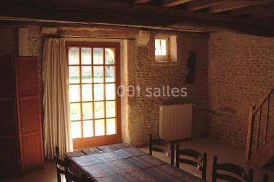 Salle à manger rustique avec murs en pierre, table en bois, chaises assorties et porte-fenêtre donnant sur l'extérieur.