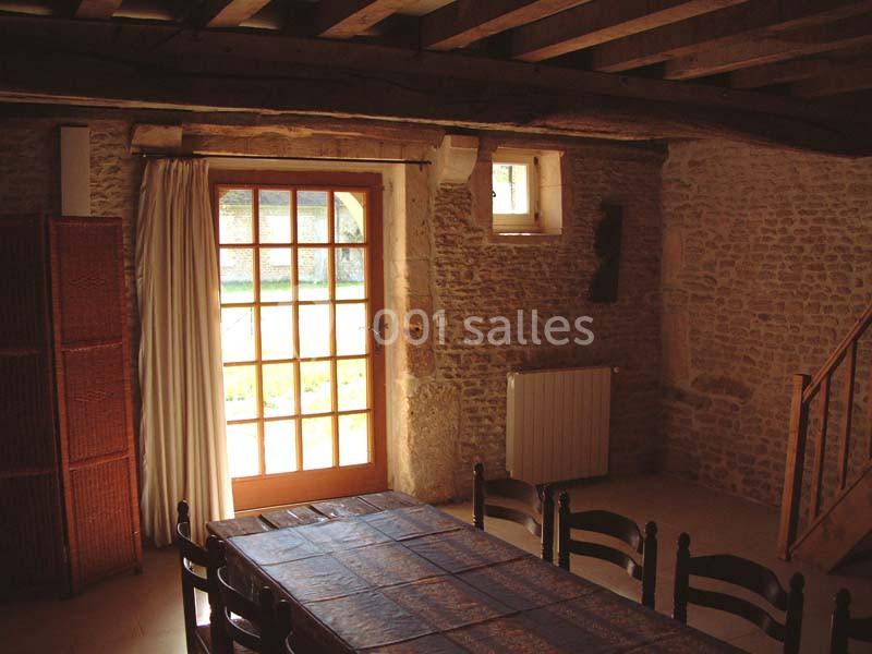 Salle à manger rustique avec murs en pierre, table en bois, chaises assorties et porte-fenêtre donnant sur l'extérieur.