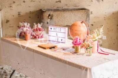 Salle en pierre avec plafond en poutres apparentes, tables dressées pour un repas, chaises blanches alignées.