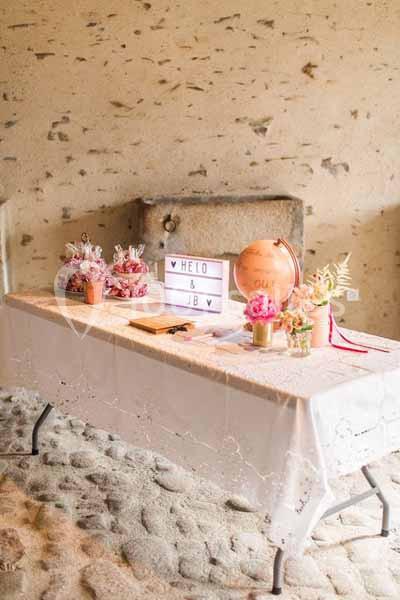 Table décorée avec des fleurs, des sachets cadeaux, une boîte lumineuse et un globe dans une pièce en pierre.
