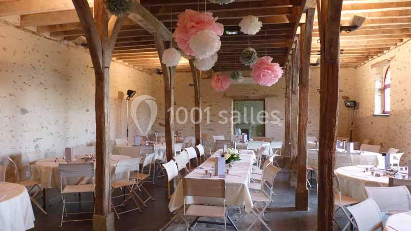 Salle de réception décorée avec des tables dressées et des pompons suspendus dans un cadre rustique en bois.
