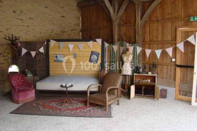 Salle en pierre avec plafond en poutres apparentes, tables dressées pour un repas, chaises blanches alignées.