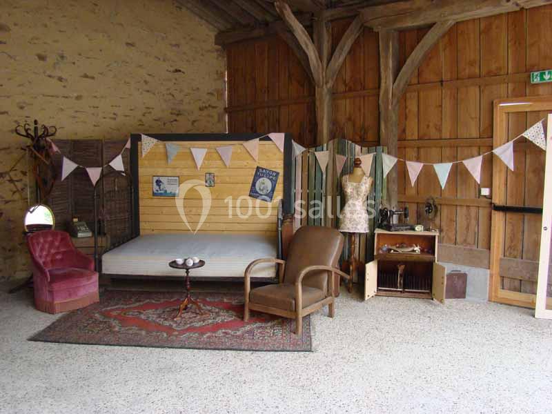 Espace intérieur rustique avec fauteuils, lit, paravent, mannequin de couture et guirlande décorative.