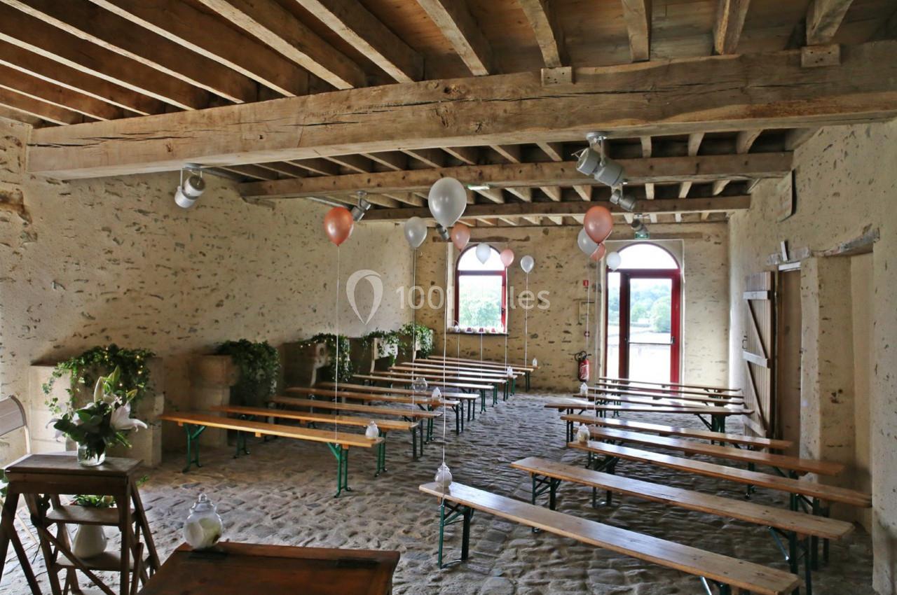 Salle rustique avec murs en pierre, poutres apparentes, bancs en bois, ballons suspendus et lumière naturelle.