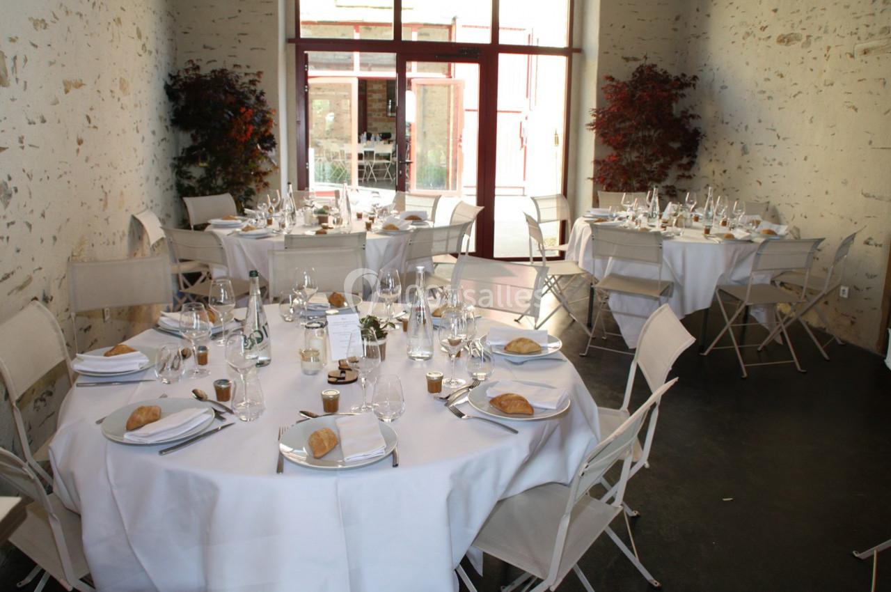 Salle de réception avec tables rondes dressées, nappes blanches, vaisselle élégante et chaises pliantes.