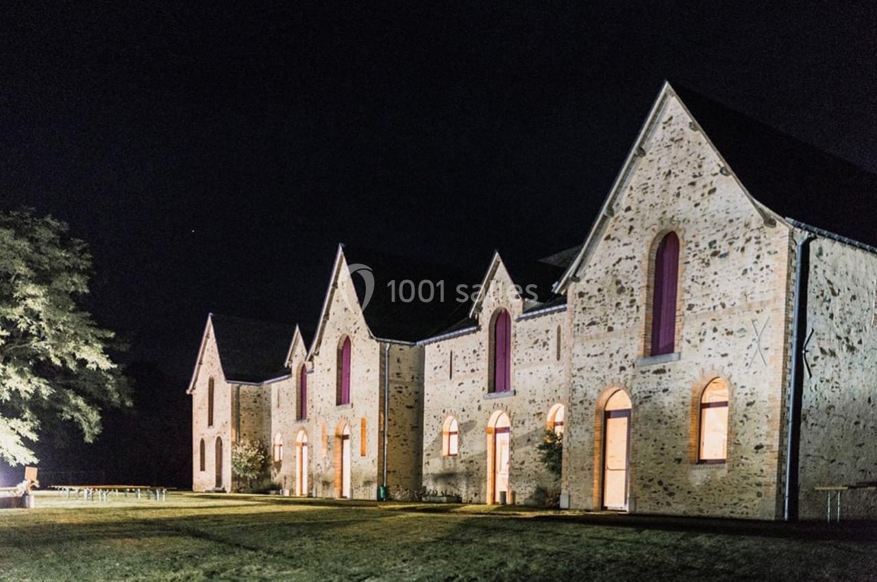 Bâtiment en pierre avec plusieurs façades éclairées et fenêtres en arc, photographié de nuit.