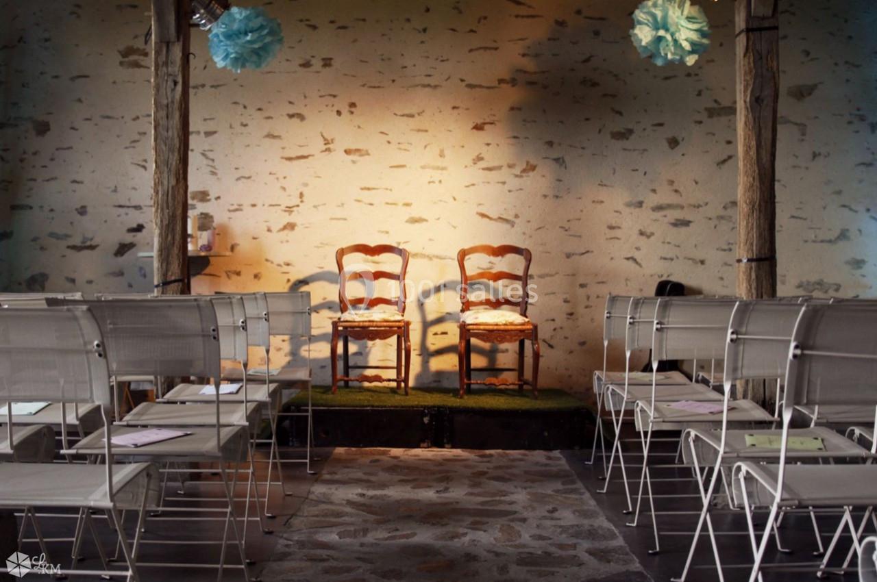 Deux chaises en bois sur une petite estrade, entourées de chaises pliantes dans une salle à murs en pierre.