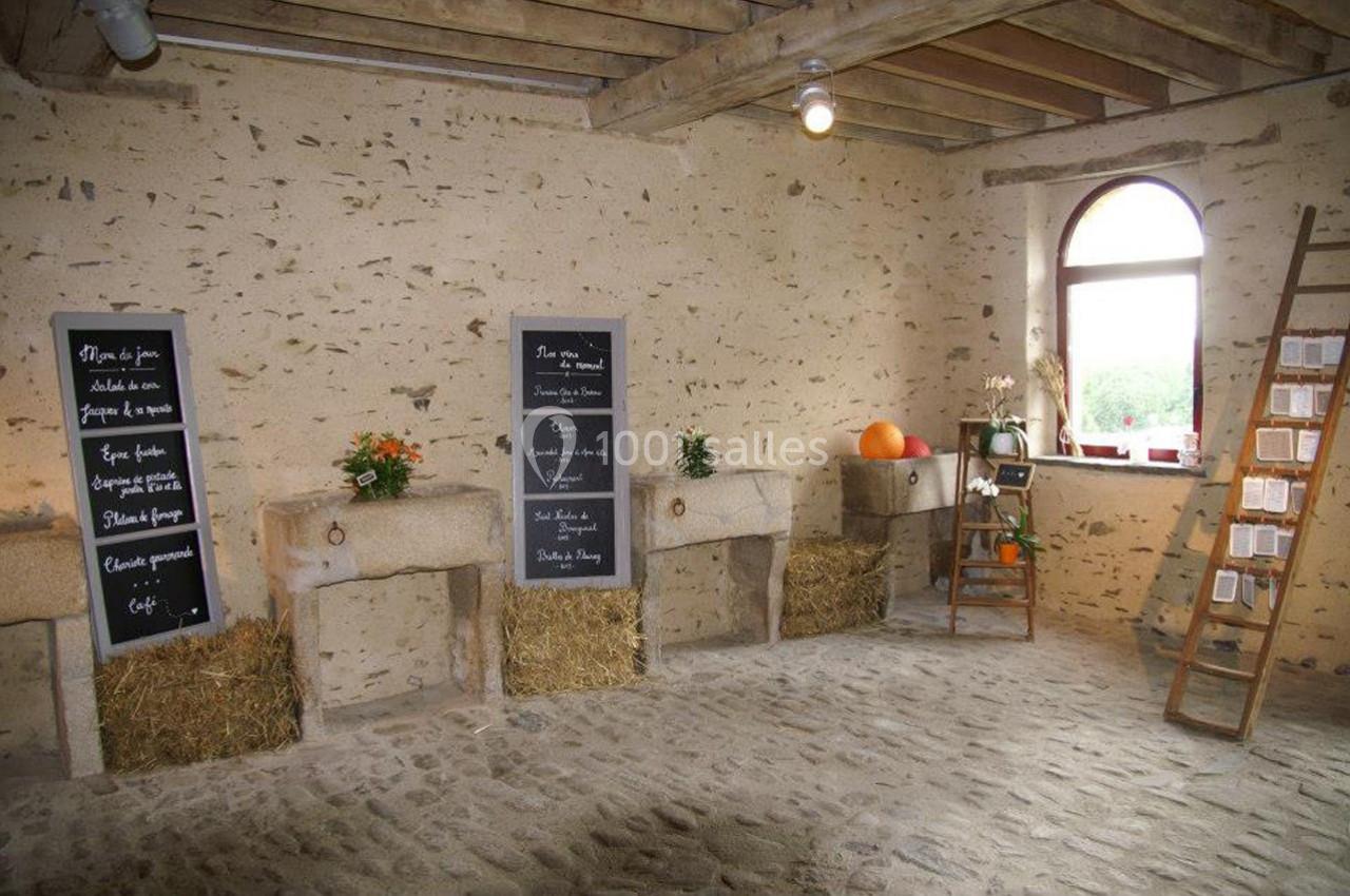 Intérieur d'une salle rustique avec murs en pierre, ardoises inscrites, bottes de paille et décorations végétales.