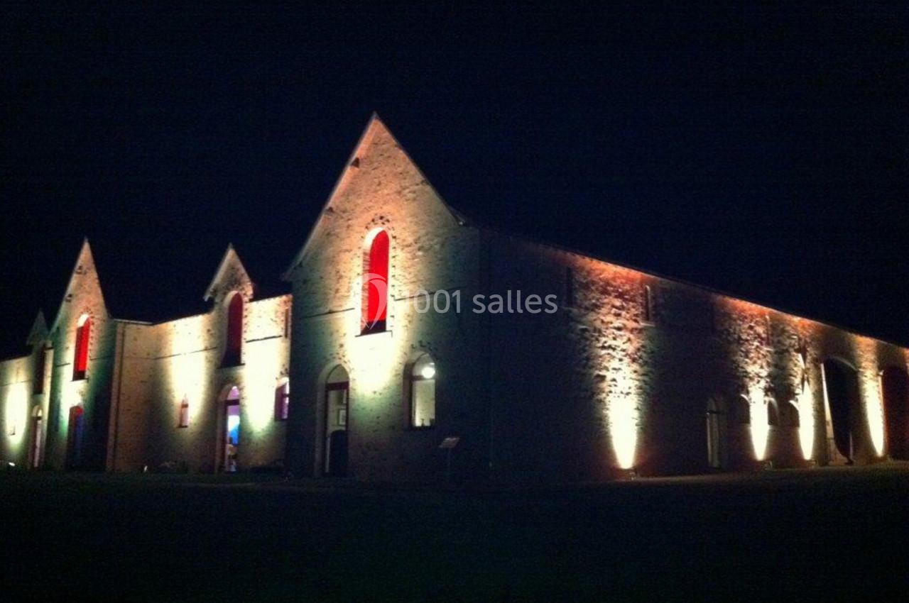 Bâtiment en pierre éclairé par des lumières colorées et blanches, photographié de nuit.