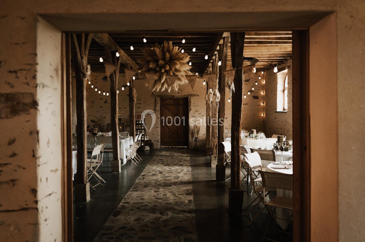 Salle rustique avec tables dressées, guirlandes lumineuses suspendues et décoration en bottes de paille au plafond.