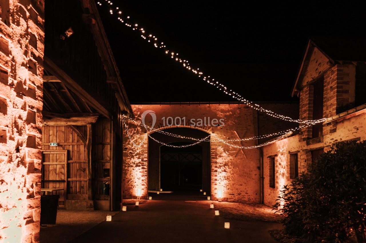Cour intérieure éclairée la nuit par des guirlandes lumineuses suspendues et des lanternes au sol.
