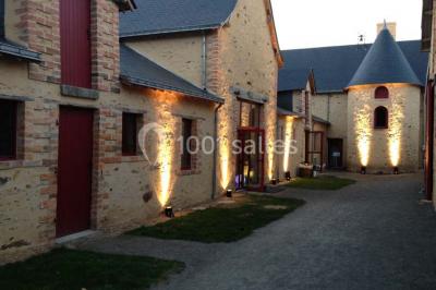 Salle en pierre avec plafond en poutres apparentes, tables dressées pour un repas, chaises blanches alignées.