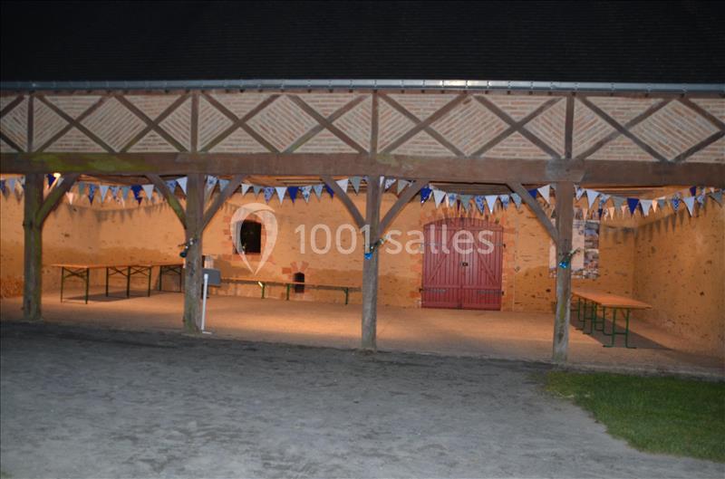 Un espace couvert en bois avec des tables et des bancs, décoré de fanions, éclairé en soirée.