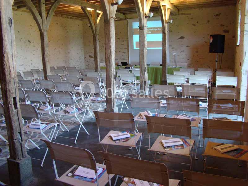 Salle de conférence rustique avec chaises pliantes disposées face à un écran de projection et une table.