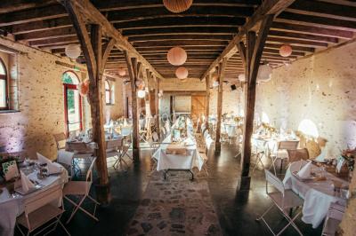 Salle de réception rustique avec tables rondes et rectangulaires dressées pour un événement, éclairage tamisé.