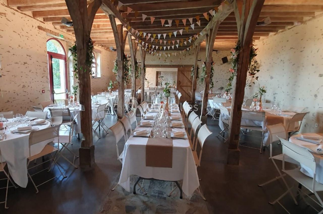 Salle de réception décorée avec des tables dressées, des guirlandes suspendues et des murs en pierre apparente.