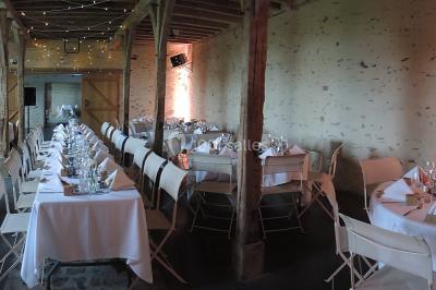 Salle de réception rustique avec tables rondes et rectangulaires dressées pour un événement, éclairage tamisé.