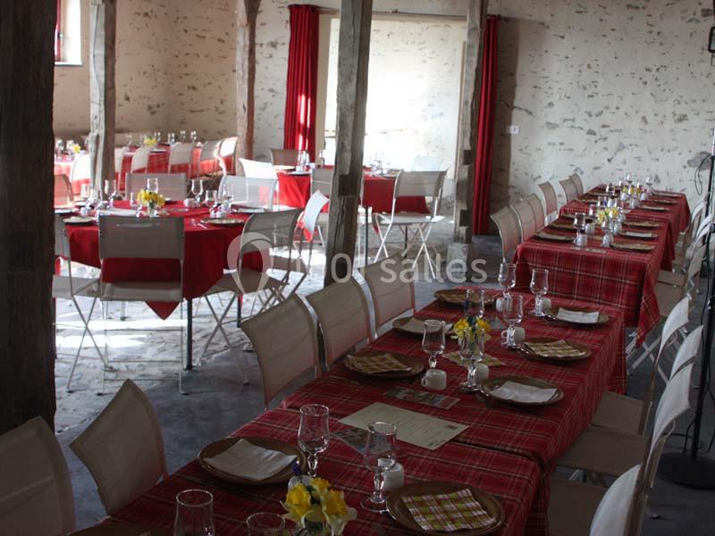 Salle de réception avec tables dressées, nappes rouges à carreaux, chaises blanches et décorations florales jaunes.