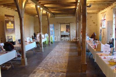 Salle de réception rustique avec tables rondes et rectangulaires dressées pour un événement, éclairage tamisé.
