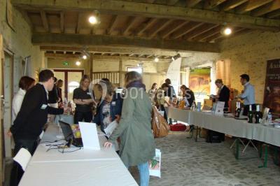 Salle de réception rustique avec tables rondes et rectangulaires dressées pour un événement, éclairage tamisé.