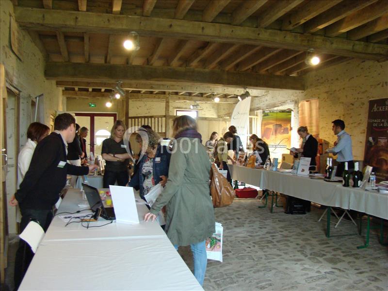 Des personnes discutent et consultent des stands dans une salle en pierre avec des tables exposant divers produits.