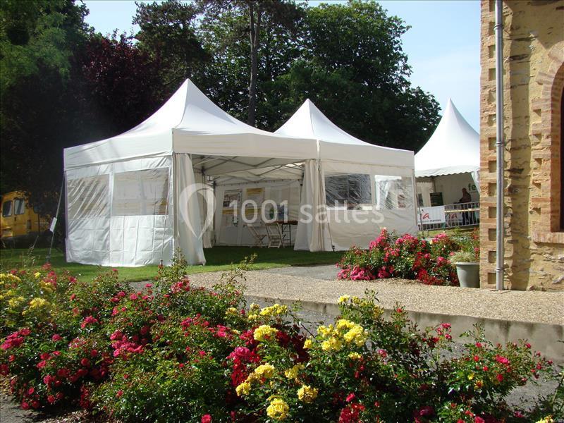 Tentes blanches installées sur une pelouse avec des panneaux d'exposition, entourées de massifs de fleurs colorées.
