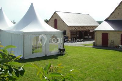 Salle de réception rustique avec tables rondes et rectangulaires dressées pour un événement, éclairage tamisé.