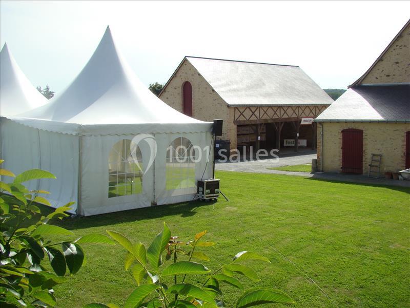 Tente blanche installée sur une pelouse, avec des bâtiments en pierre et une cour en arrière-plan.