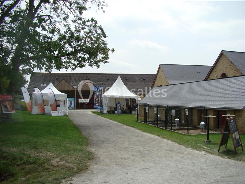 Chemin menant à des bâtiments en pierre avec des stands, une tente blanche et des enclos extérieurs.