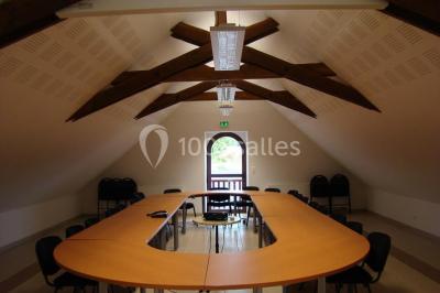 Salle de réception rustique avec tables rondes et rectangulaires dressées pour un événement, éclairage tamisé.