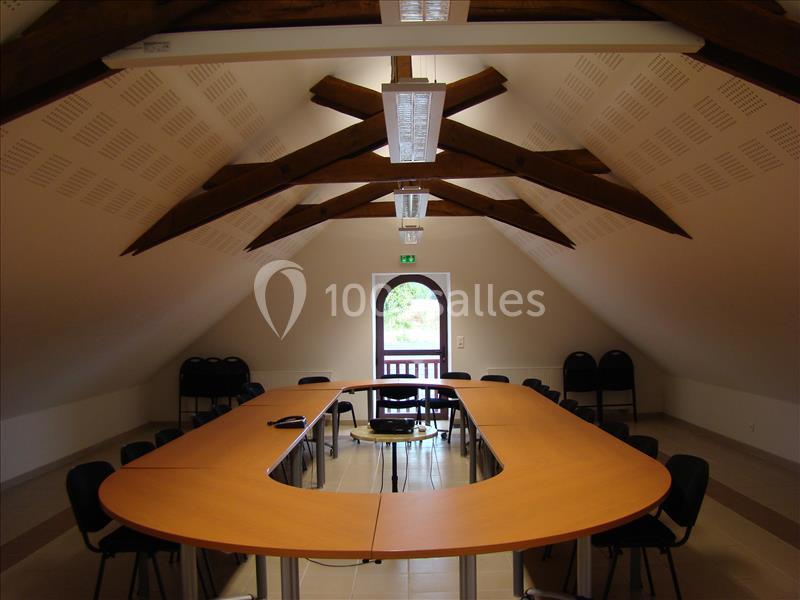 Salle de réunion sous combles avec poutres apparentes, table en U, chaises noires et lumière naturelle.