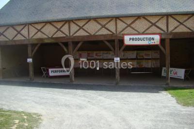 Salle de réception rustique avec tables rondes et rectangulaires dressées pour un événement, éclairage tamisé.