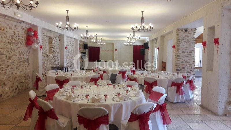 Salle de réception décorée avec des tables rondes, nappes blanches et nœuds rouges sur les chaises.