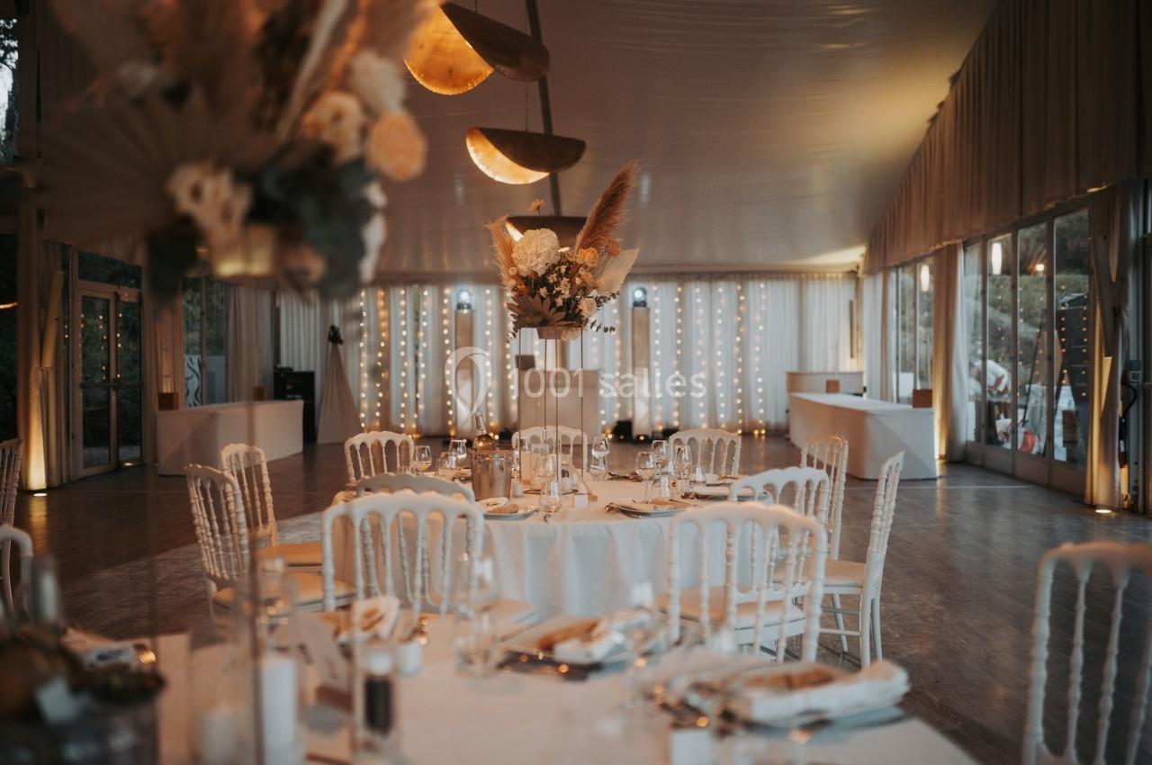 Salle de réception décorée avec des tables rondes, chaises blanches et éclairage chaleureux.