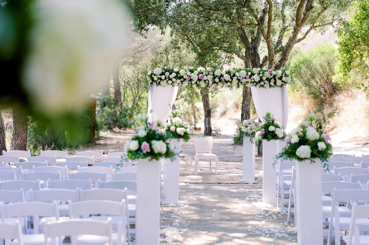 Allée extérieure décorée de fleurs blanches et roses menant à une arche pour une cérémonie de mariage.