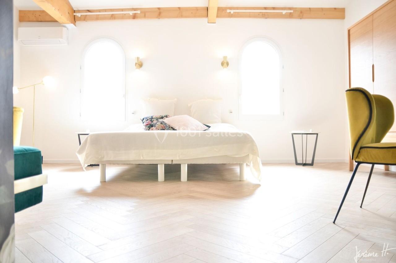 Chambre lumineuse avec lit double, parquet en chevrons, murs blancs, poutres apparentes et mobilier moderne.