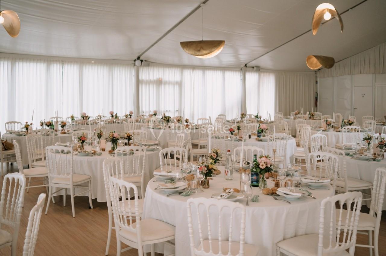 Salle de réception décorée avec des tables rondes, nappes blanches, chaises assorties et arrangements floraux.