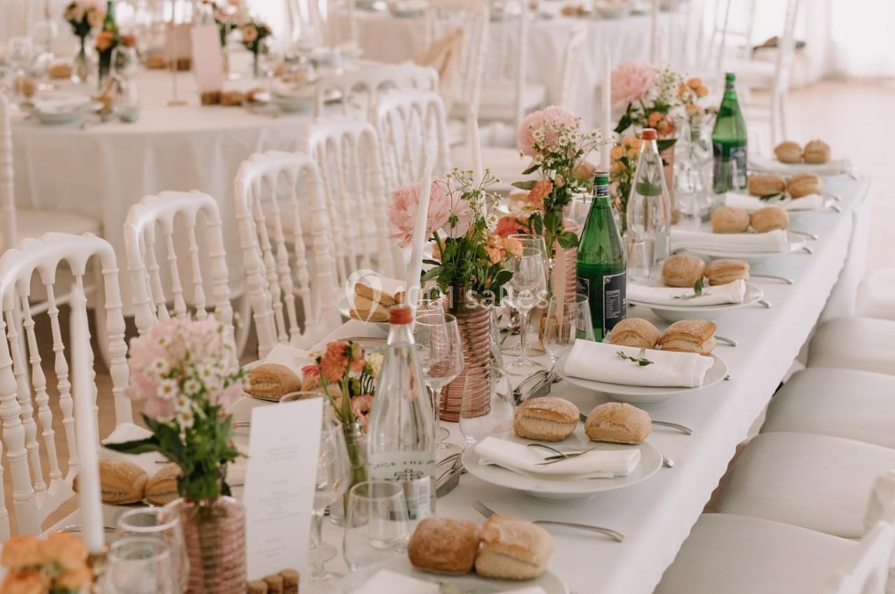 Table de réception élégamment dressée avec nappes blanches, fleurs, bouteilles d'eau et vaisselle disposée pour un repas.