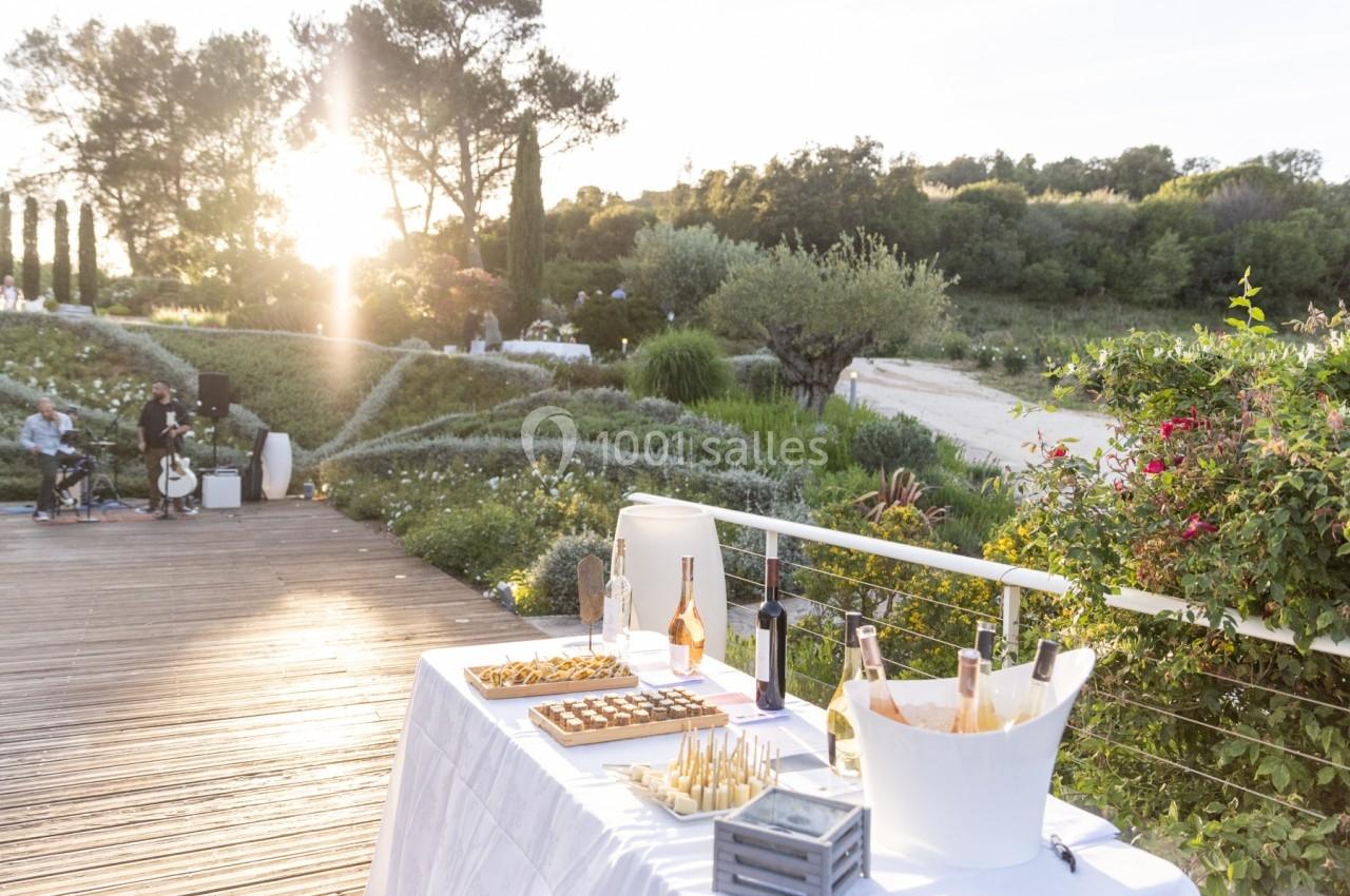 Table dressée en extérieur avec boissons et amuse-bouches, entourée de végétation et baignée par une lumière de coucher de…