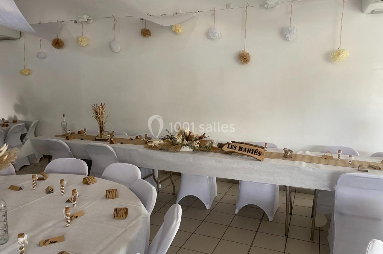 Salle décorée pour un mariage avec tables dressées, nappes blanches, chaises houssées et ornements floraux naturels.