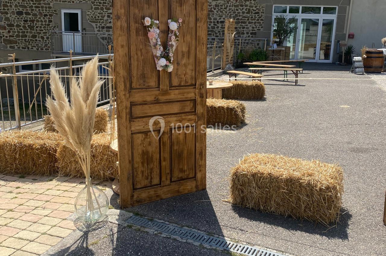 Porte en bois décorée de fleurs, entourée de bottes de paille et de pampas, dans une cour extérieure ensoleillée.