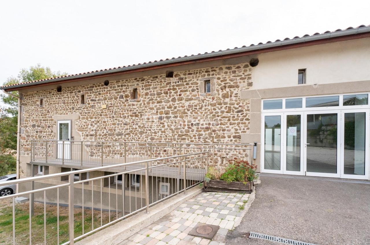 Façade d'un bâtiment en pierre avec des fenêtres modernes et une entrée vitrée, entouré d'un espace pavé.