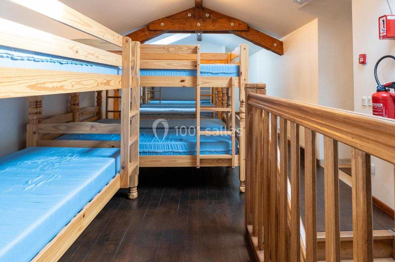 Dortoir avec lits superposés en bois, matelas bleus, parquet sombre et lumière naturelle provenant d'une fenêtre de toit.