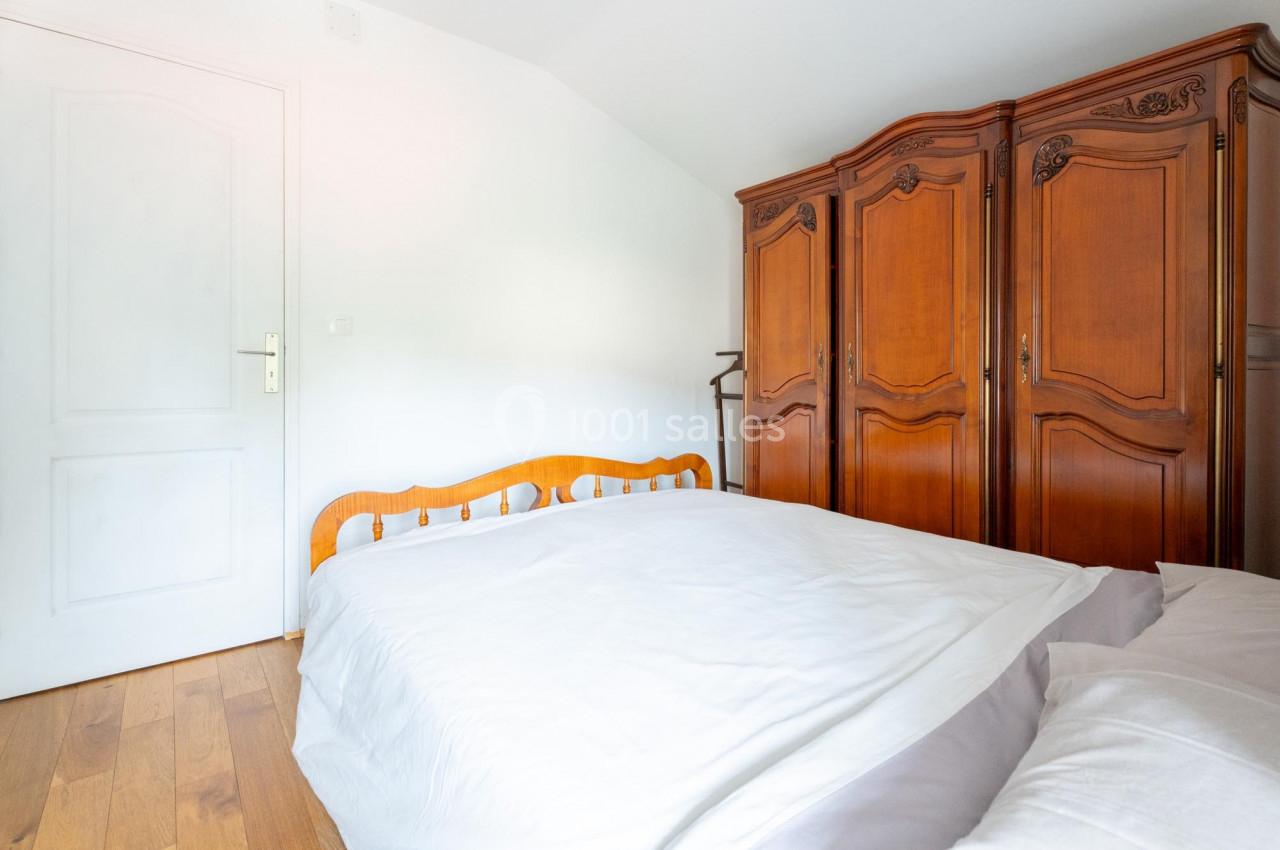 Chambre avec un lit double, draps blancs, parquet en bois et une grande armoire en bois sculpté.