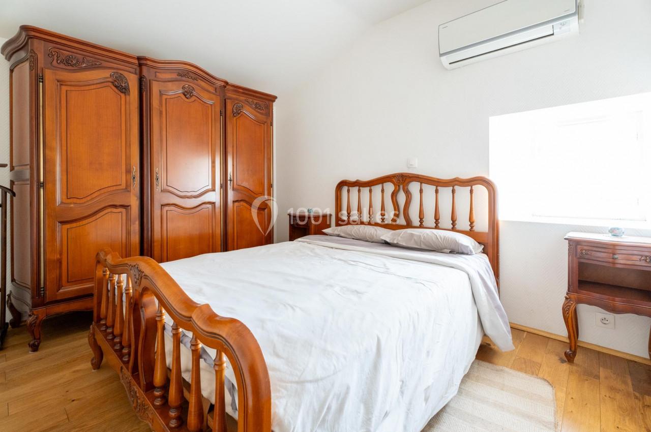 Chambre lumineuse avec lit en bois sculpté, armoire assortie, parquet clair et climatisation murale.