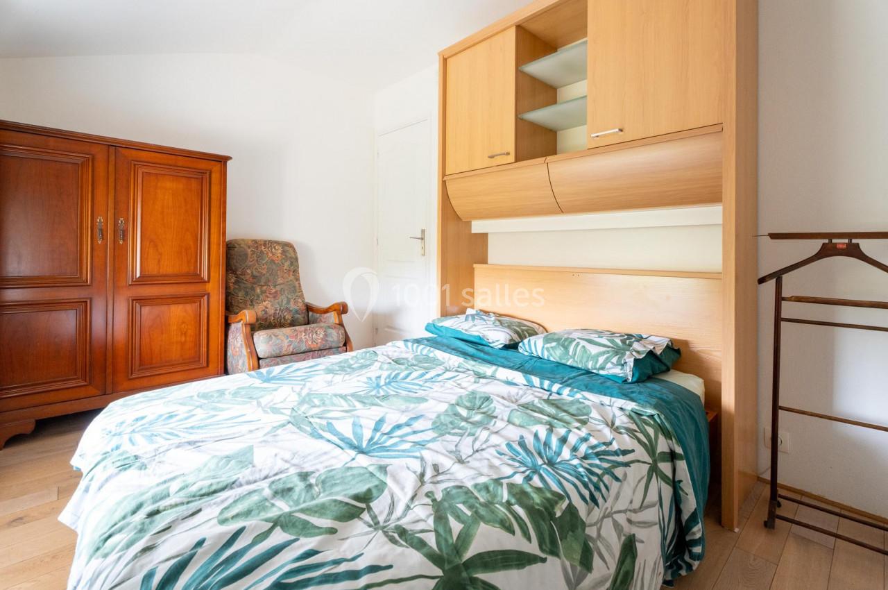 Chambre lumineuse avec lit double, housse de couette à motifs végétaux, armoire en bois et fauteuil rembourré.