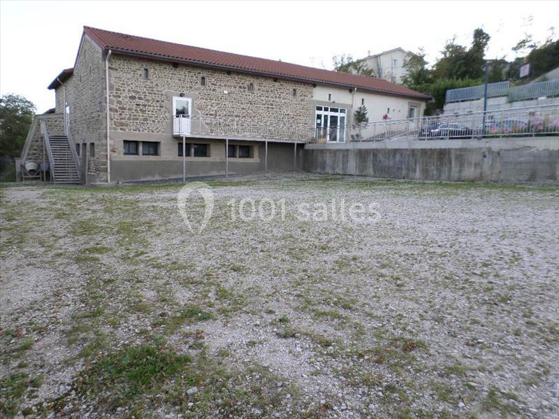 Bâtiment en pierre avec toit rouge, escalier extérieur et espace dégagé en gravier devant.