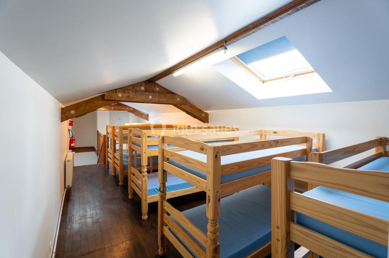 Dortoir sous les combles avec lits superposés en bois, éclairé par une fenêtre de toit.