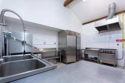 Cuisine professionnelle avec équipements en inox, comprenant un réfrigérateur, une hotte, un four et des plans de travail.